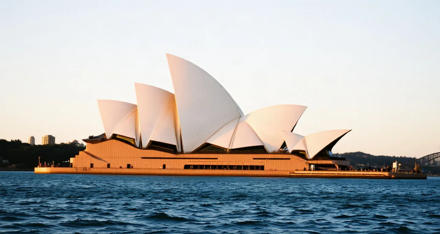 Sydney harbour and the opera house roofs across calm water at golden hour