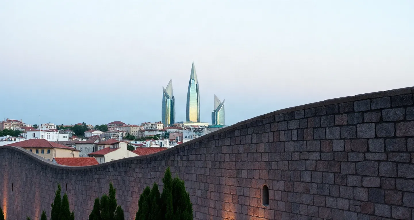Stone walls of Baku old city with flame-shaped towers in the distance at dusk