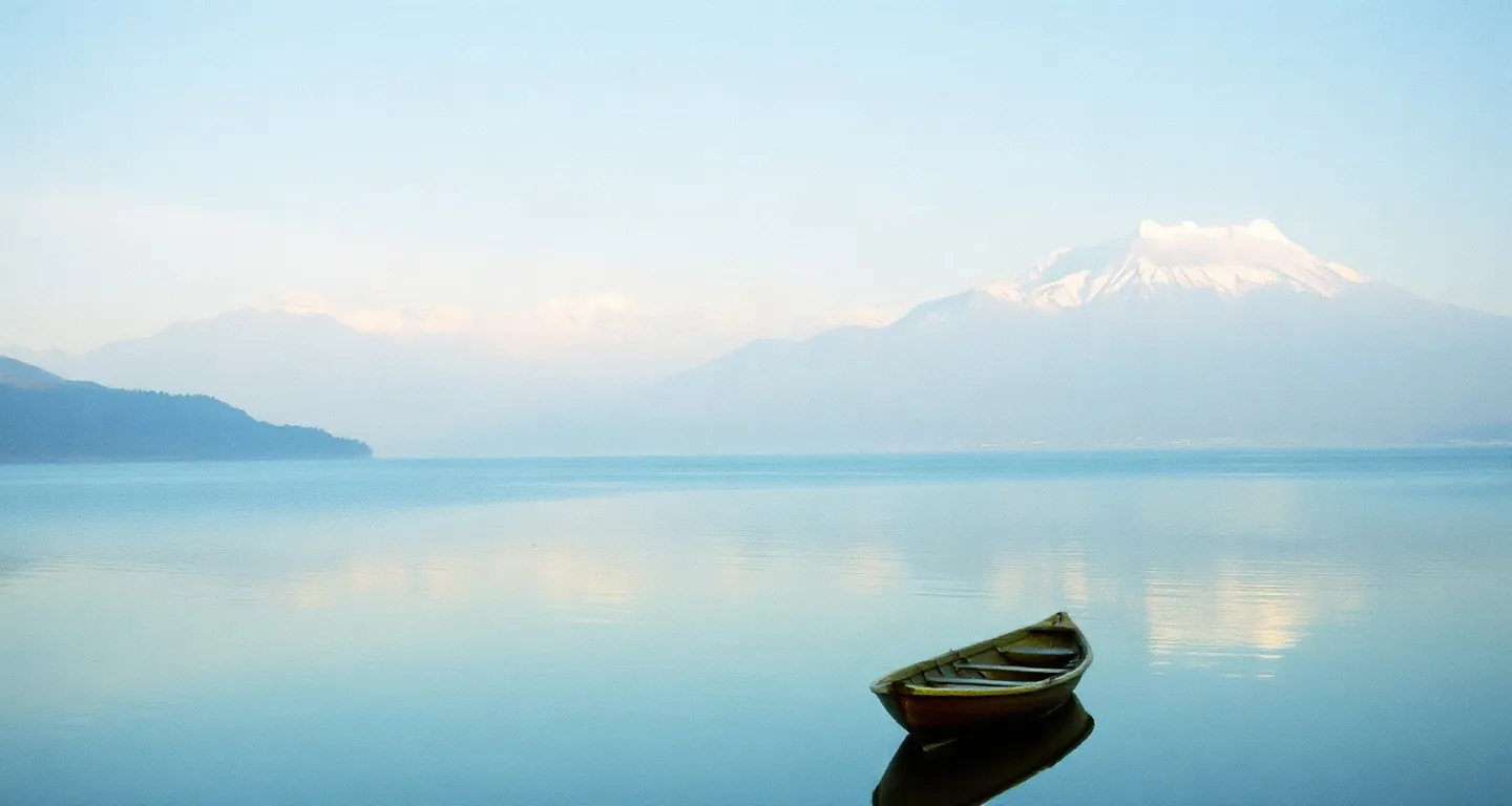 Snow-capped Himalayan peaks above a calm lake with a wooden boat in Pokhara